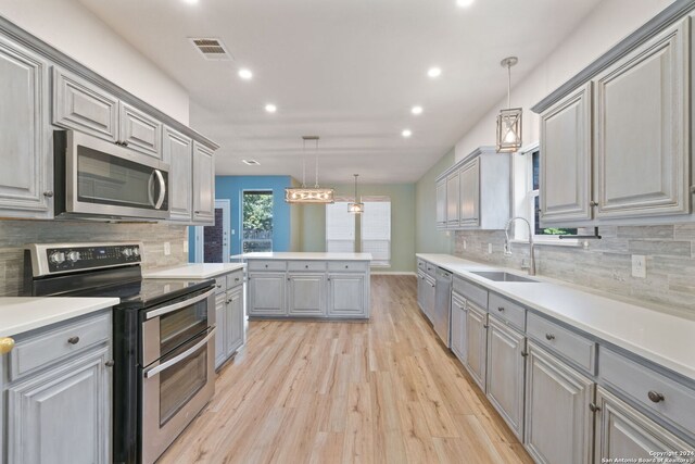 kitchen with gray cabinetry, sink, stainless steel appliances, pendant lighting, and light hardwood / wood-style floors