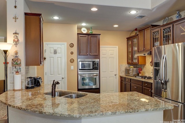 kitchen featuring light stone countertops, backsplash, stainless steel appliances, and sink