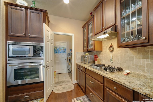 kitchen featuring light stone countertops, appliances with stainless steel finishes, tasteful backsplash, hardwood / wood-style flooring, and independent washer and dryer