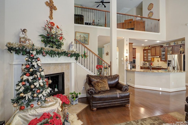 living room featuring ceiling fan, a fireplace, a towering ceiling, and dark hardwood / wood-style floors