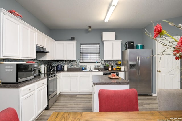 kitchen with tasteful backsplash, white cabinets, hardwood / wood-style floors, a kitchen island, and appliances with stainless steel finishes