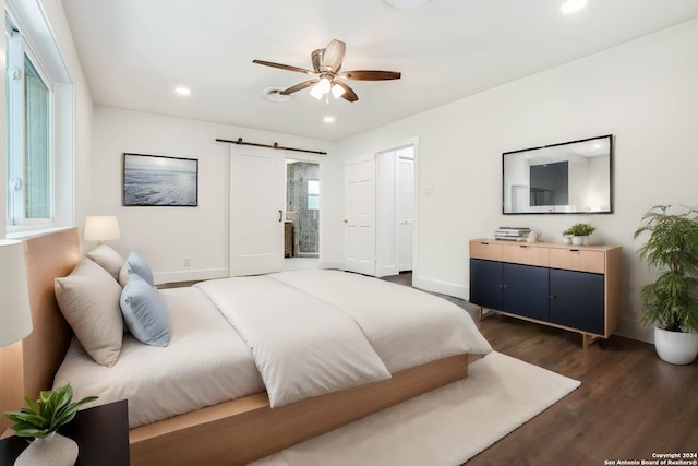 bedroom featuring a barn door, dark hardwood / wood-style floors, ceiling fan, and connected bathroom