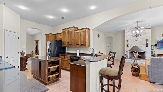 kitchen with kitchen peninsula, stainless steel refrigerator with ice dispenser, a large fireplace, sink, and a kitchen island