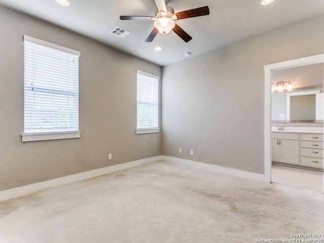 unfurnished bedroom featuring ceiling fan, light colored carpet, and ensuite bath