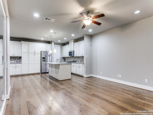 kitchen featuring stainless steel appliances, white cabinetry, an island with sink, backsplash, and pendant lighting