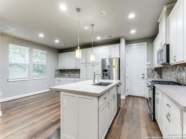 kitchen featuring appliances with stainless steel finishes, pendant lighting, white cabinetry, and a kitchen island with sink