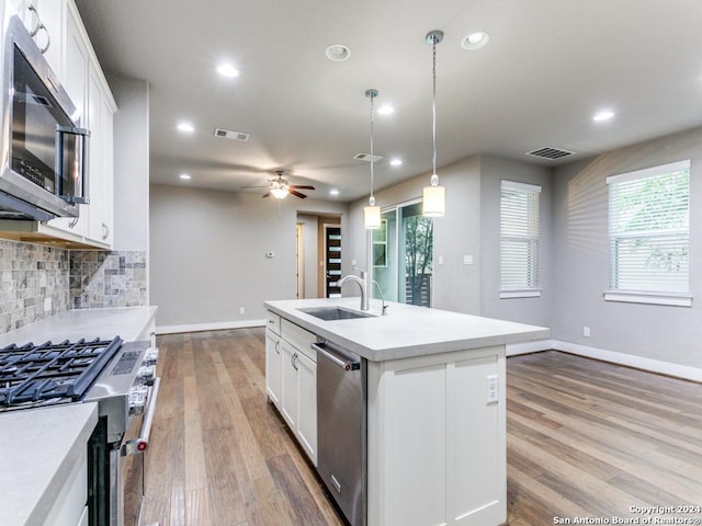 kitchen with hanging light fixtures, stainless steel appliances, a kitchen island with sink, white cabinetry, and sink