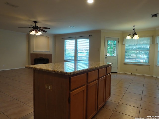 kitchen with a tile fireplace, a kitchen island, pendant lighting, light tile patterned floors, and ceiling fan with notable chandelier