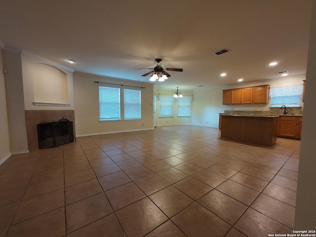 unfurnished living room featuring ceiling fan with notable chandelier, crown molding, sink, light tile patterned floors, and a fireplace