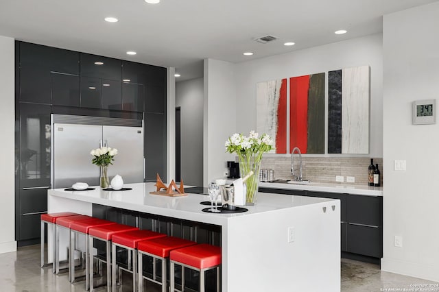 kitchen featuring sink, built in refrigerator, a breakfast bar area, decorative backsplash, and a kitchen island