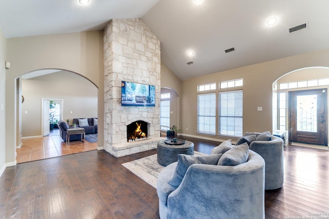 living room with a stone fireplace, dark hardwood / wood-style flooring, and high vaulted ceiling