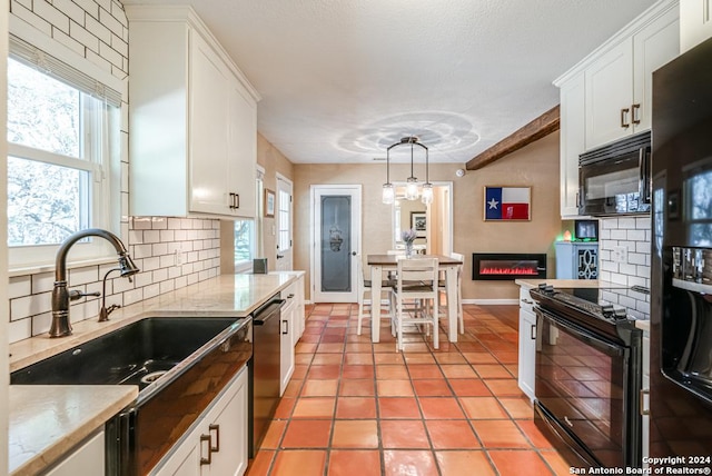 kitchen with white cabinets, a glass covered fireplace, hanging light fixtures, black appliances, and a sink