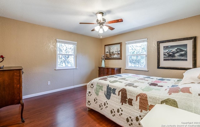 bedroom featuring a textured wall, dark wood finished floors, baseboards, and ceiling fan