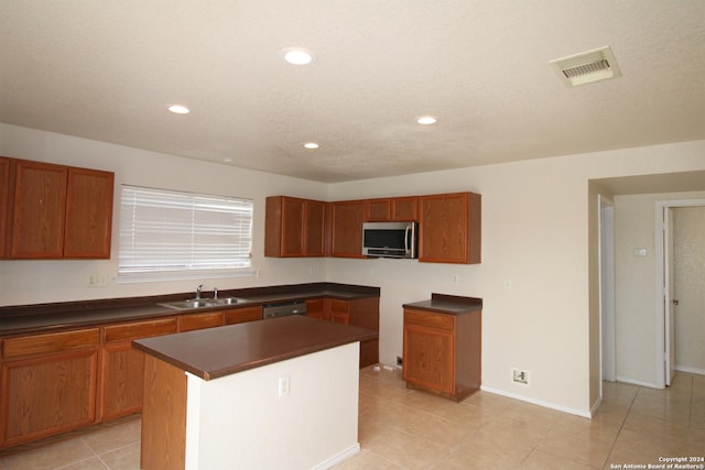 kitchen featuring sink, light tile patterned floors, a textured ceiling, dishwashing machine, and a kitchen island