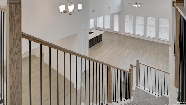 stairway with ceiling fan with notable chandelier, a high ceiling, wood finished floors, and visible vents