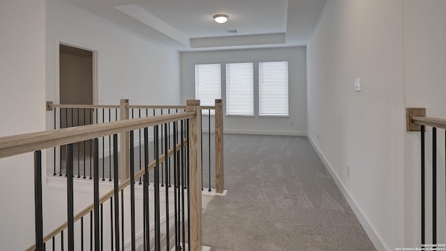 hall with carpet, a tray ceiling, baseboards, and an upstairs landing