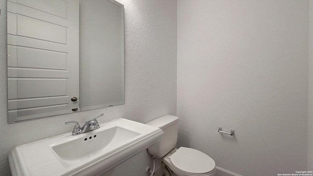 half bath featuring a textured wall, a sink, and toilet