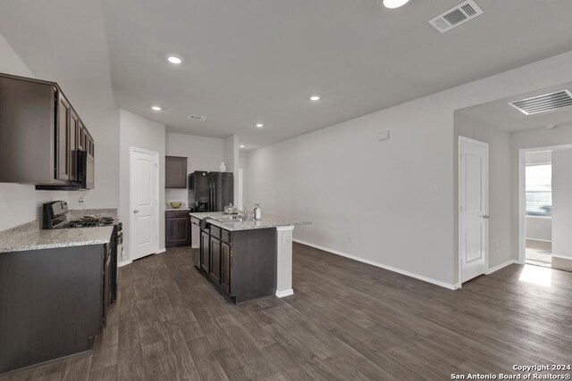 kitchen with dark hardwood / wood-style floors, black appliances, a kitchen island with sink, dark brown cabinetry, and light stone counters