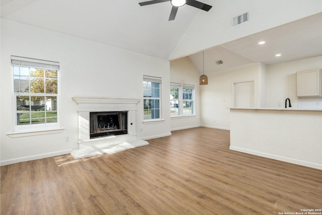 unfurnished living room with ceiling fan, light hardwood / wood-style flooring, high vaulted ceiling, and a healthy amount of sunlight