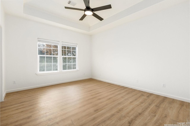 empty room with a tray ceiling, ceiling fan, and light hardwood / wood-style flooring