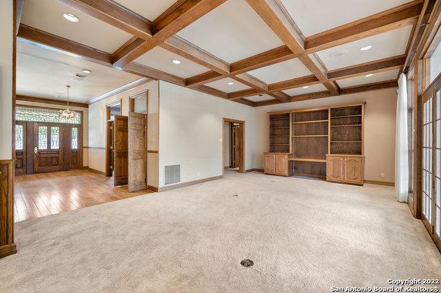 unfurnished living room with hardwood / wood-style floors, coffered ceiling, crown molding, beamed ceiling, and a chandelier