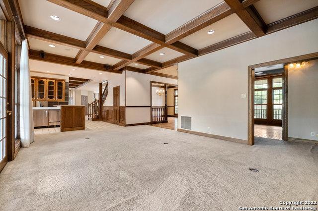 unfurnished living room with beamed ceiling, light colored carpet, and coffered ceiling