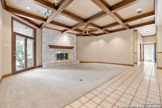 unfurnished living room with coffered ceiling, ceiling fan, a fireplace, beamed ceiling, and light tile patterned flooring