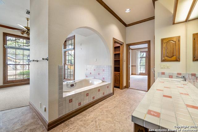 bathroom with ceiling fan, tiled tub, sink, and a wealth of natural light