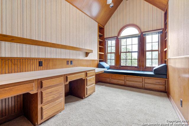 carpeted home office with built in shelves, built in desk, ceiling fan, and lofted ceiling