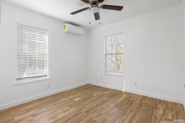 unfurnished room featuring light wood-type flooring, an AC wall unit, a wealth of natural light, and ceiling fan