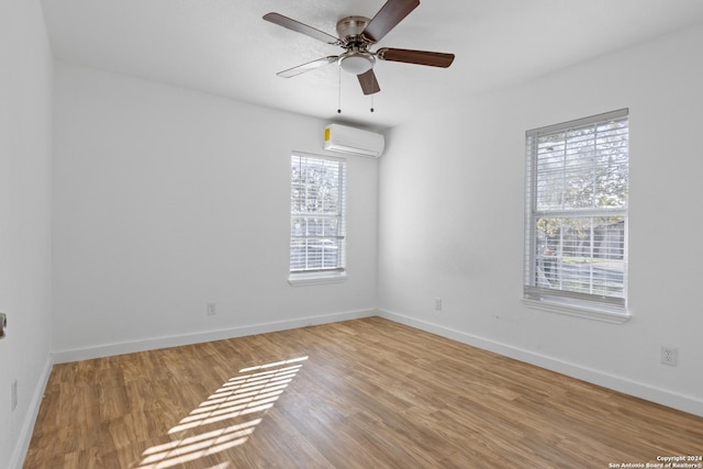 empty room with ceiling fan, plenty of natural light, a wall mounted air conditioner, and light wood-type flooring