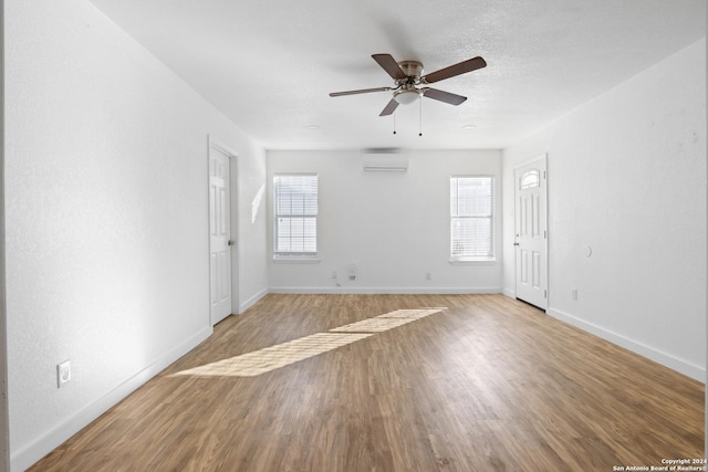 unfurnished room featuring light wood-type flooring, a wall unit AC, and a wealth of natural light