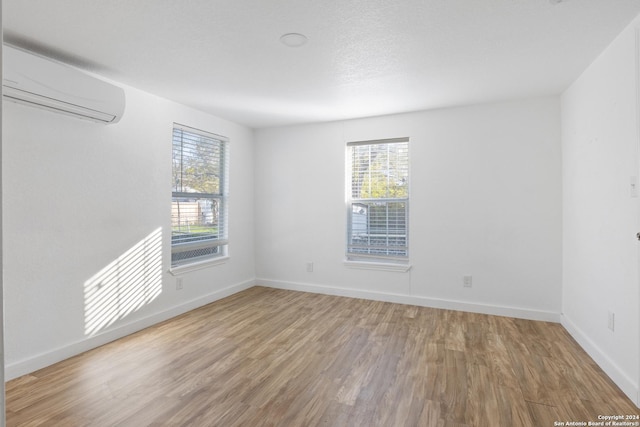 unfurnished room featuring a wall mounted AC, a healthy amount of sunlight, and hardwood / wood-style flooring