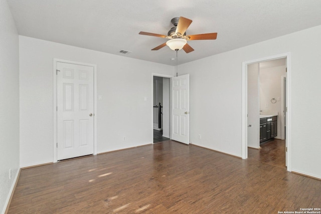 unfurnished bedroom featuring ceiling fan, ensuite bathroom, and dark wood-type flooring