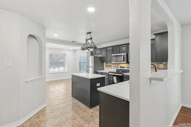 kitchen with light stone countertops, light tile patterned floors, backsplash, a kitchen island, and appliances with stainless steel finishes