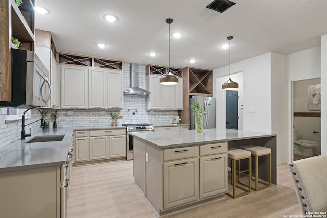 kitchen featuring sink, hanging light fixtures, stainless steel appliances, wall chimney range hood, and a kitchen island