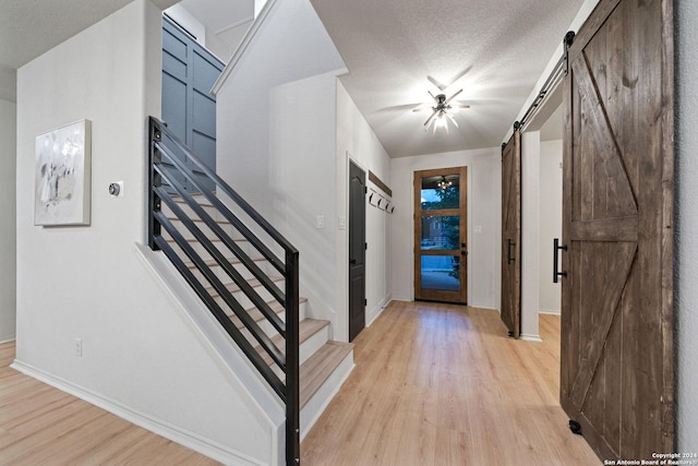 foyer featuring ceiling fan, a barn door, light hardwood / wood-style floors, and a textured ceiling