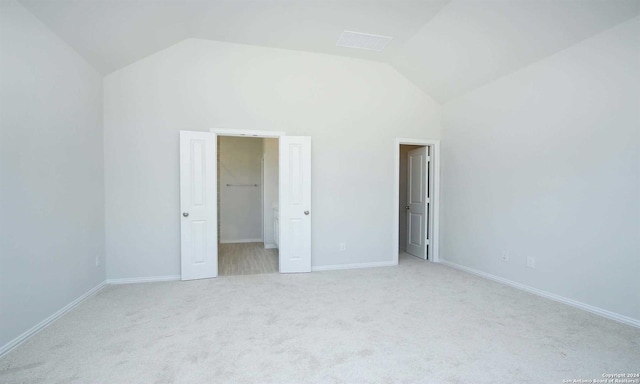 unfurnished bedroom featuring light carpet, a closet, a spacious closet, and vaulted ceiling