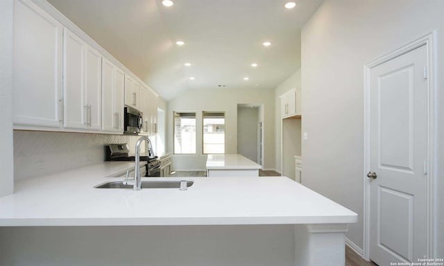 kitchen featuring kitchen peninsula, white cabinets, stainless steel appliances, and vaulted ceiling