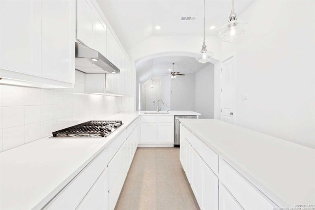 kitchen featuring wall chimney exhaust hood, stainless steel appliances, decorative light fixtures, white cabinetry, and lofted ceiling