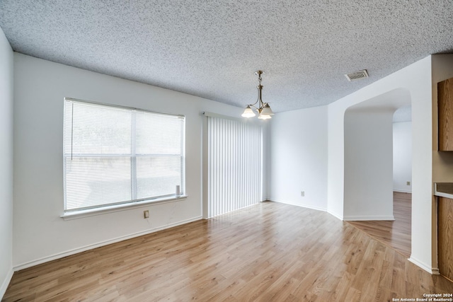 unfurnished room with light hardwood / wood-style floors, a textured ceiling, and a notable chandelier