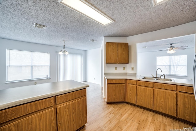 kitchen featuring pendant lighting, ceiling fan with notable chandelier, sink, light hardwood / wood-style flooring, and a textured ceiling