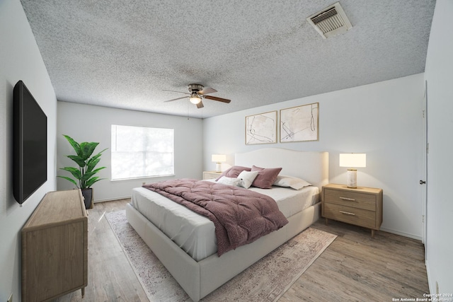 bedroom with ceiling fan, light hardwood / wood-style flooring, and a textured ceiling