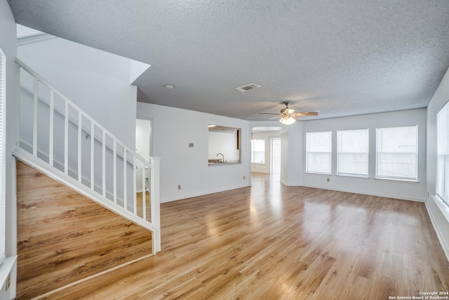 unfurnished living room with ceiling fan, light hardwood / wood-style floors, and a textured ceiling