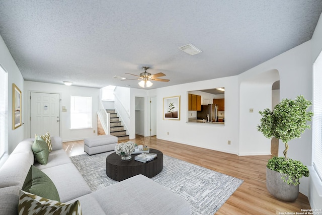 living room featuring ceiling fan, a textured ceiling, and light hardwood / wood-style flooring