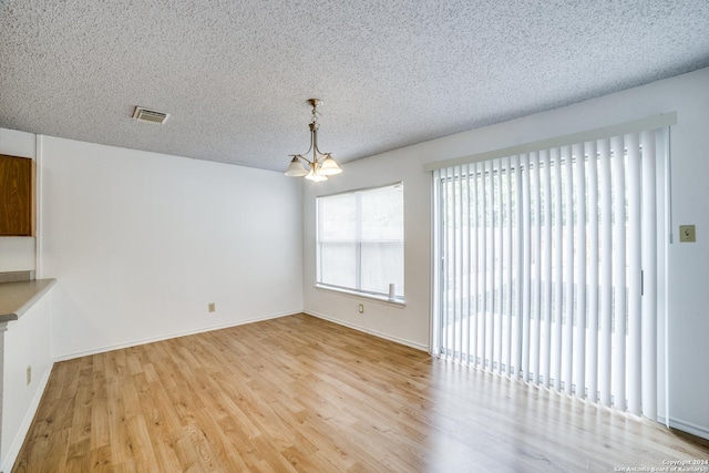 unfurnished dining area featuring an inviting chandelier, a textured ceiling, and light hardwood / wood-style flooring