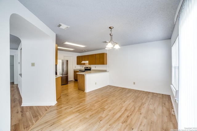 kitchen featuring a textured ceiling, appliances with stainless steel finishes, light hardwood / wood-style floors, kitchen peninsula, and a chandelier