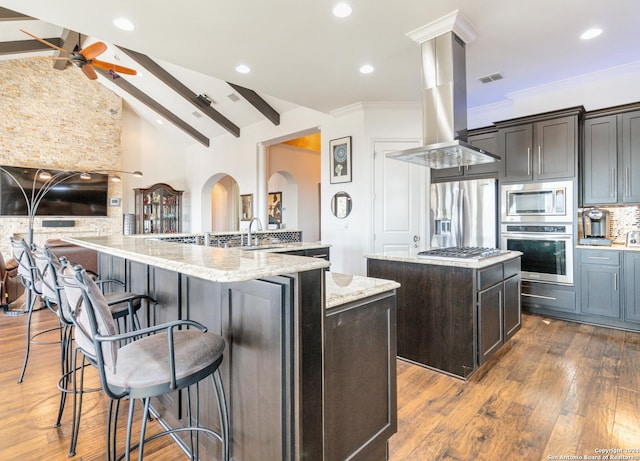 kitchen featuring beamed ceiling, island exhaust hood, a kitchen island with sink, dark brown cabinets, and appliances with stainless steel finishes