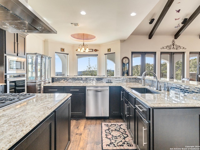 kitchen with pendant lighting, sink, wall chimney exhaust hood, light stone countertops, and appliances with stainless steel finishes