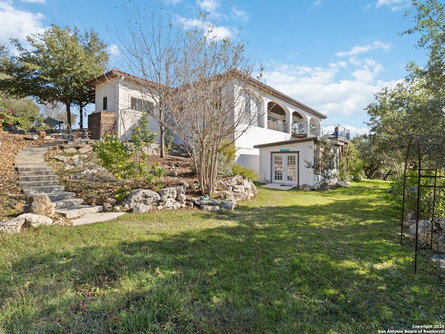 back of property with french doors, a balcony, and a lawn